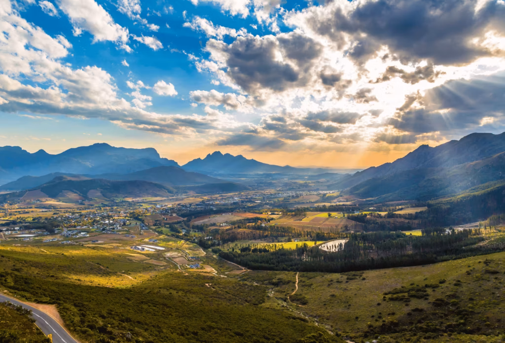 Het landschap bij Franshhoek in Zuid-Afrika met de bergen op de achtergrond en de zon die door de wolken schijnt.